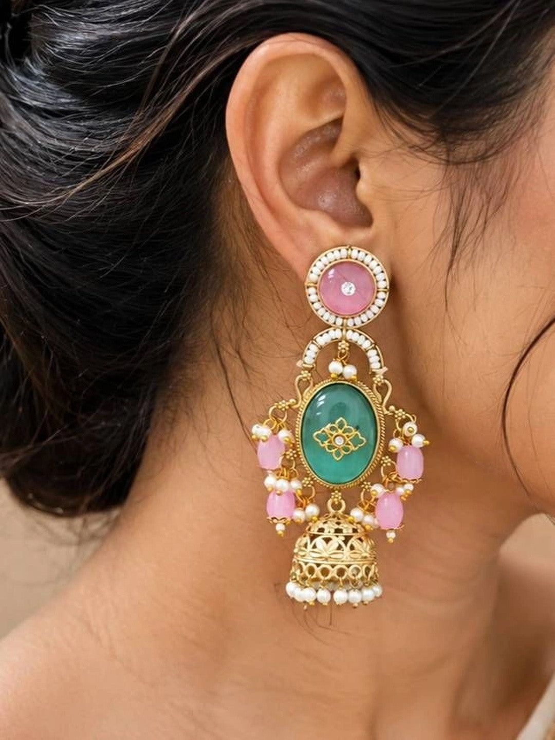 Front and back view of gold-plated jhumka earrings with pink and green stones on white surface