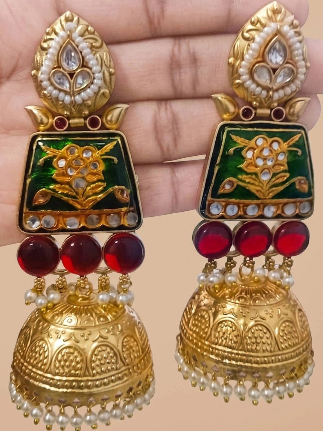 Pair of Meenakari kundan jhumkas held in a hand, front view showing both earrings with red glass beads and gold dome