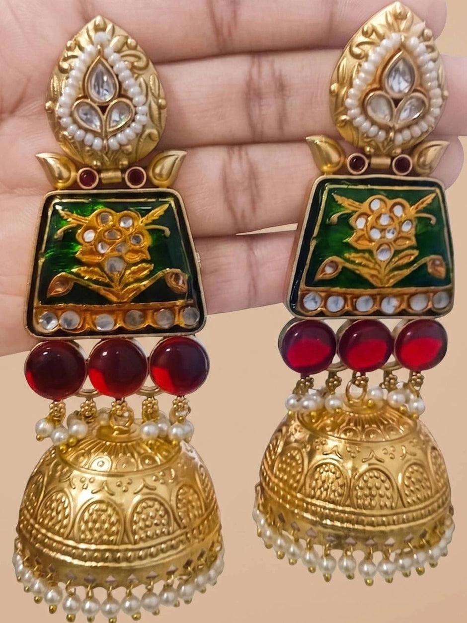 Pair of Meenakari kundan jhumkas held in a hand, front view showing both earrings with red glass beads and gold dome
