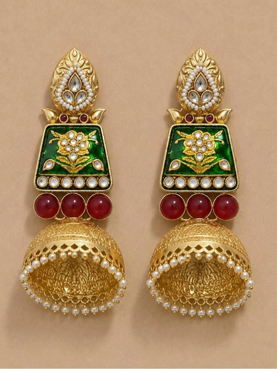Both jhumka earrings laid flat on a beige surface, displaying leaf stud tops, green enamel panels and lattice dome bells