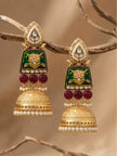 Pair of gold-plated kundan jhumkas hanging from a dry wooden branch against a warm beige background