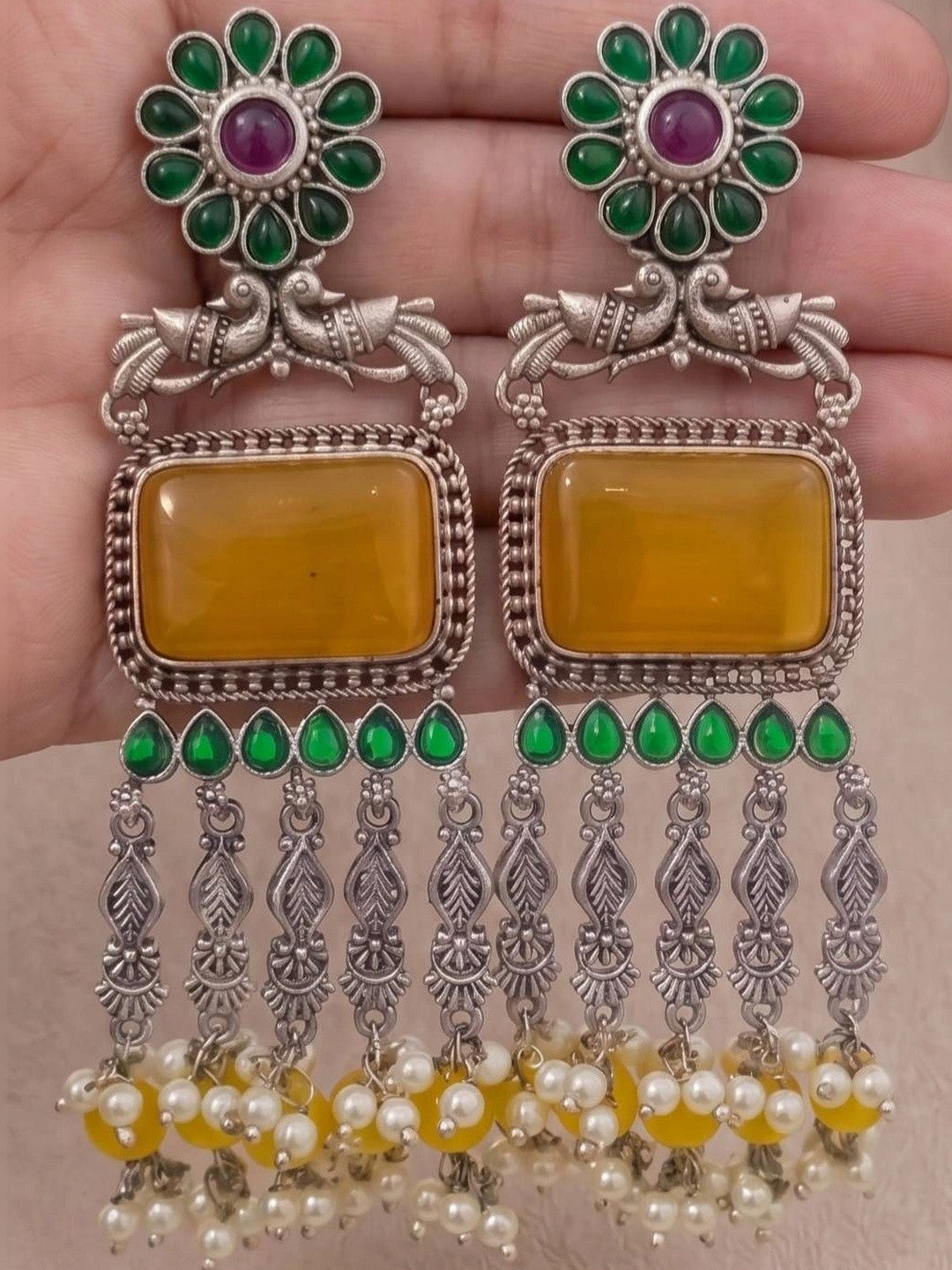 Both oxidised silver chandbali earrings held in palm showing full front detail of green stones, yellow centre and pearl drops