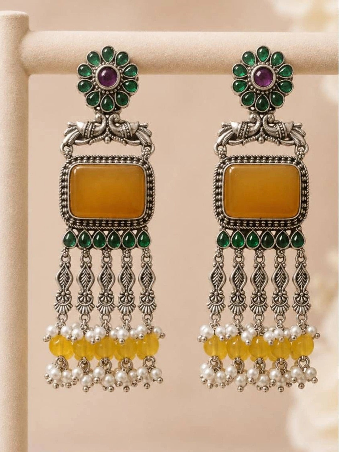 Two oxidised silver chandbali earrings standing upright on display rack showing full length and cascading pearl and yellow bead drops