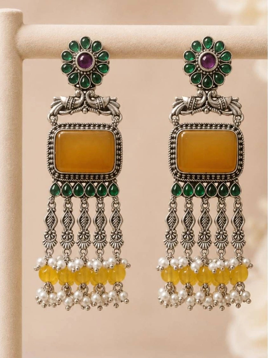 Two oxidised silver chandbali earrings standing upright on display rack showing full length and cascading pearl and yellow bead drops