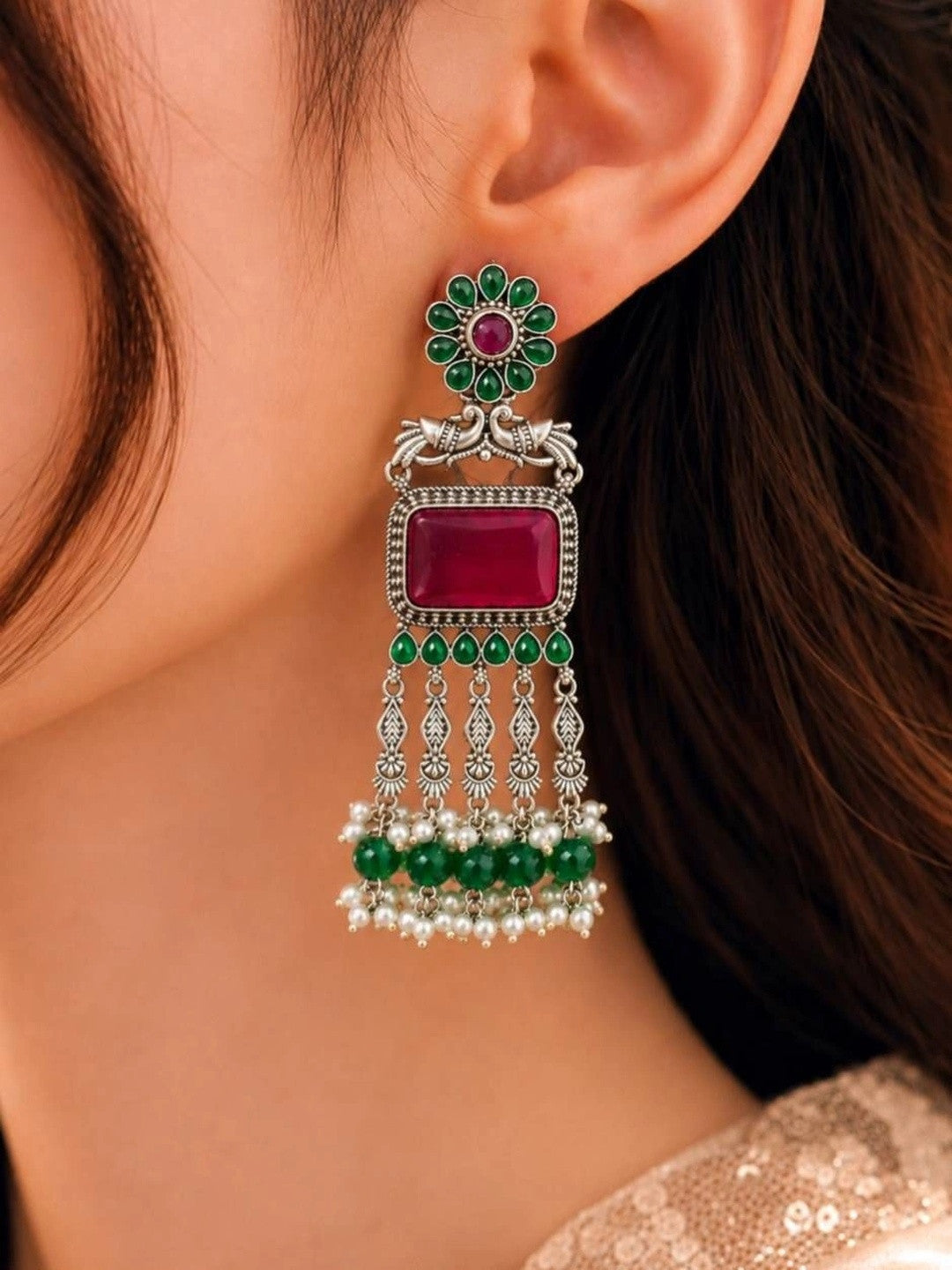 Oxidised silver chandbali earring with ruby-red stone and green pearl tassels worn on ear