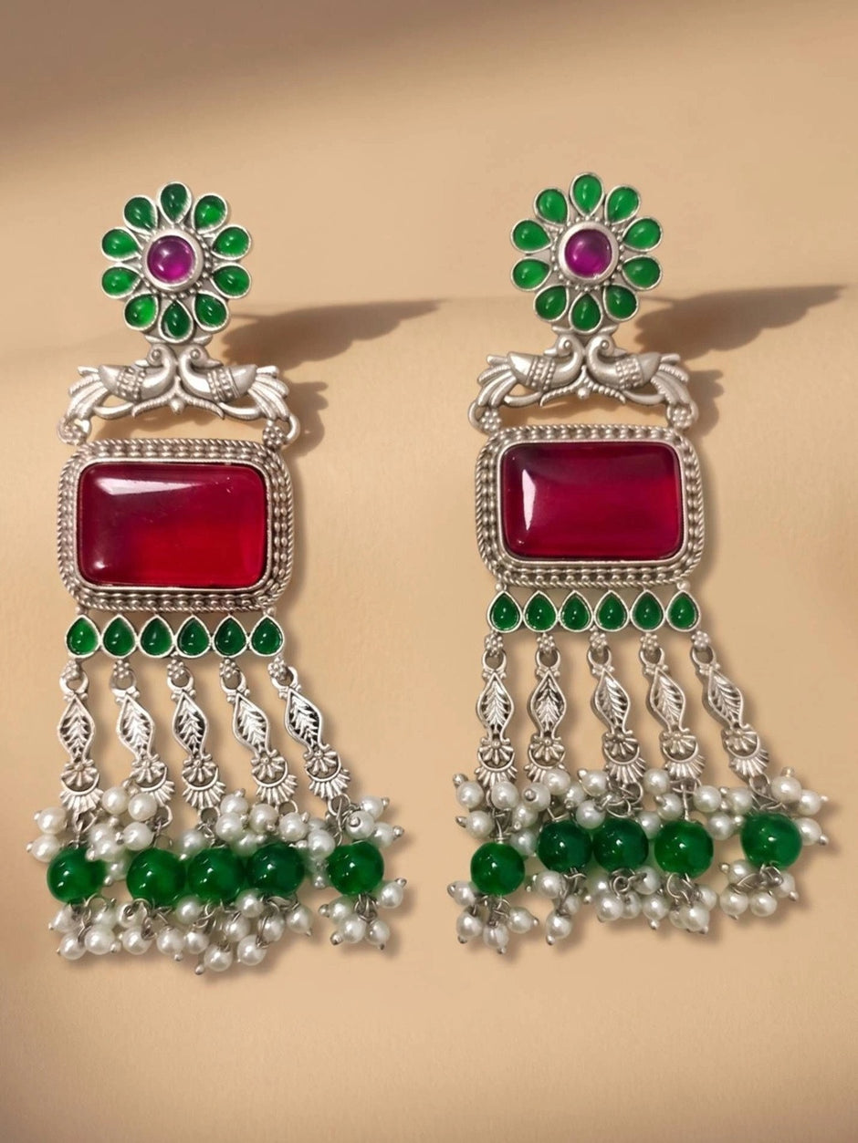 Pair of oxidised silver chandbali earrings with ruby stone, green beads and white pearl drops on beige surface