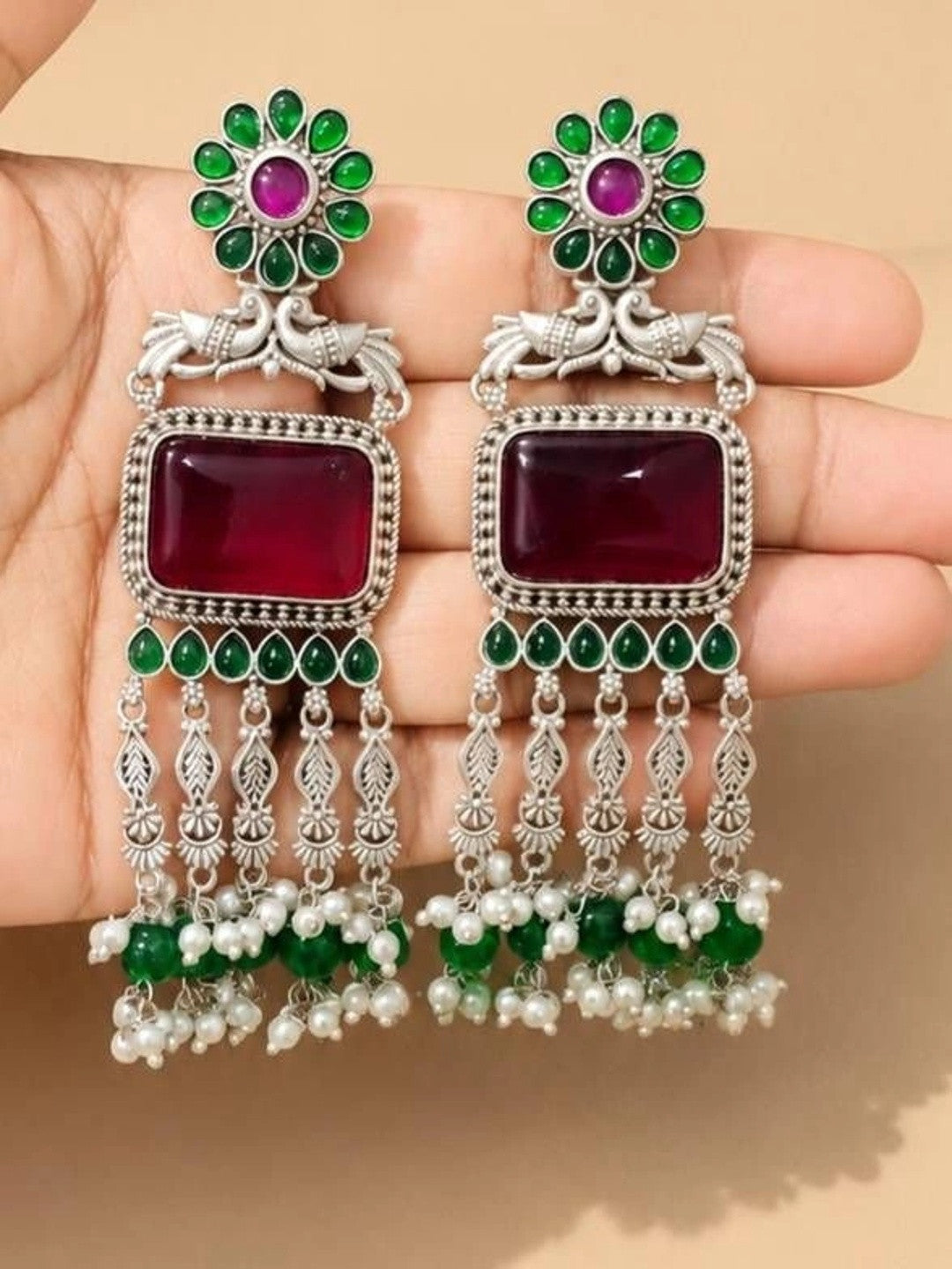 Both chandbali earrings held in palm showing ruby stone, peacock motif and layered pearl tassel detail