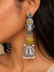 Woman wearing a long oxidised silver jhumka earring with yellow stone and green accents against dark hair
