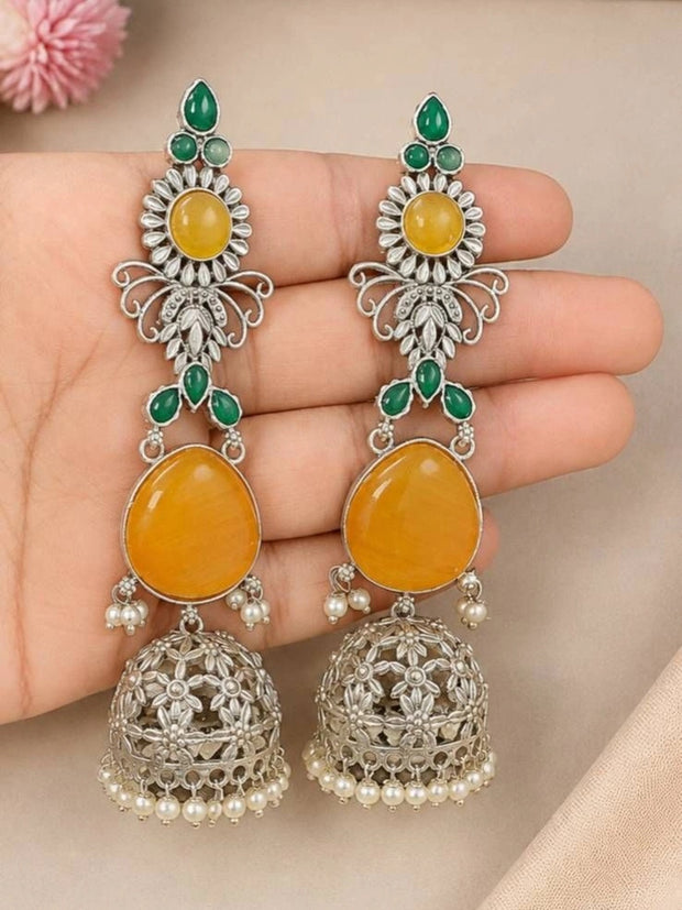 Pair of oxidised silver jhumka earrings with yellow cabochons and green stones resting on an open palm