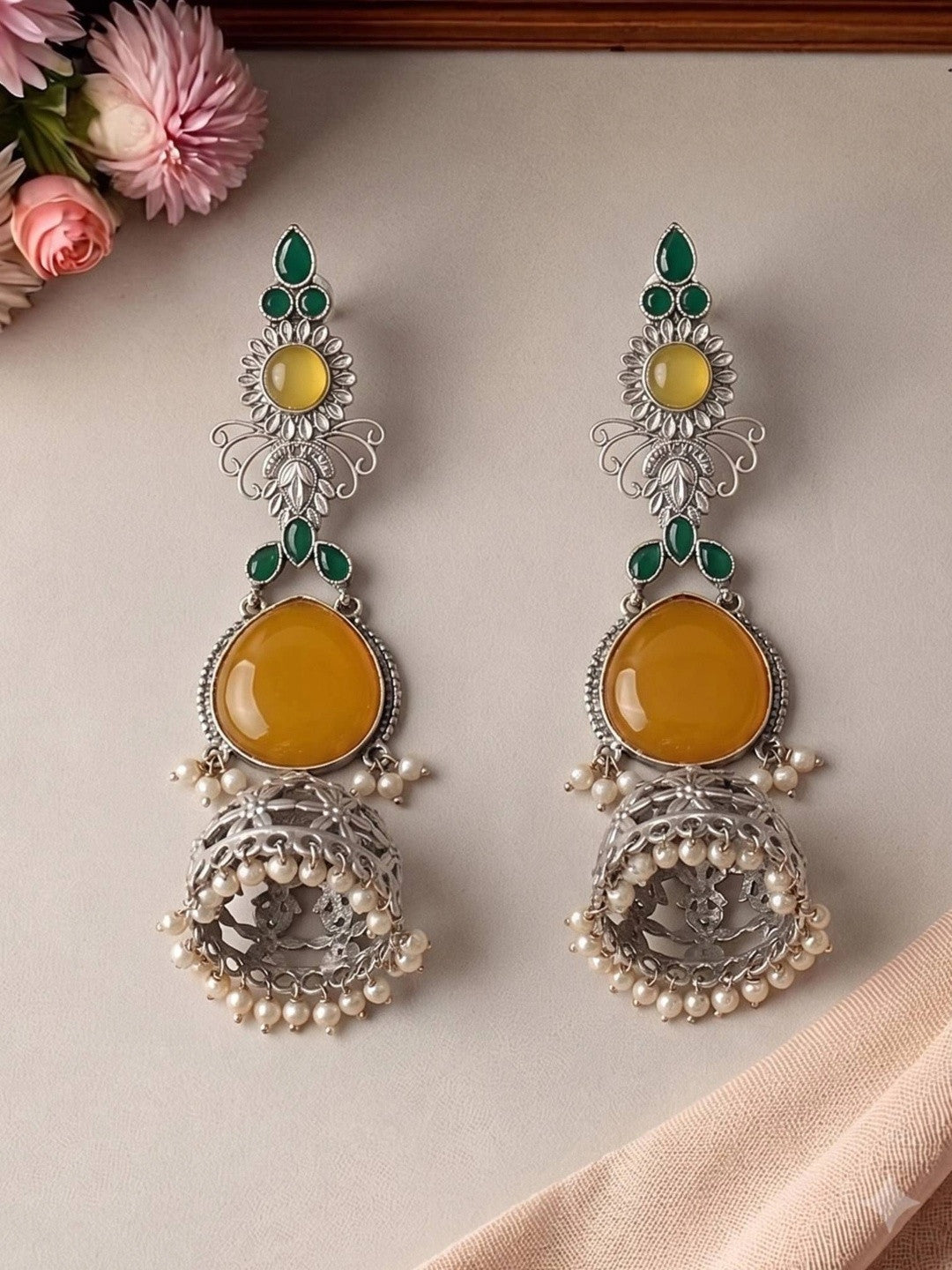 Two oxidised silver jhumka earrings laid flat showing floral filigree dome and pearl drop detail