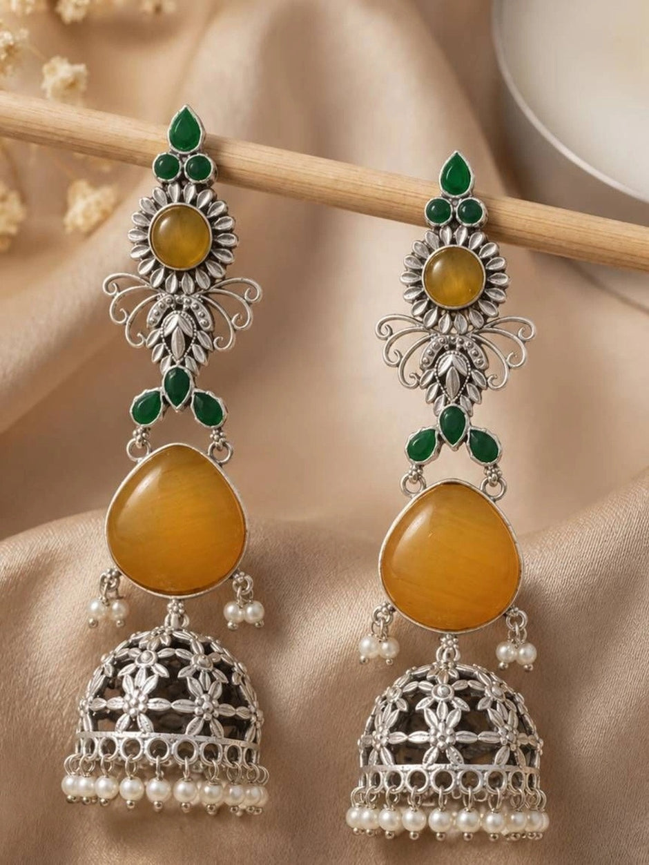 Pair of long silver jhumka earrings with amber yellow stones hanging from a wooden rod against draped fabric
