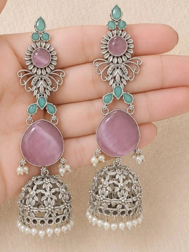 Pair of oxidised silver jhumka earrings with pink cabochon and mint stones held in palm