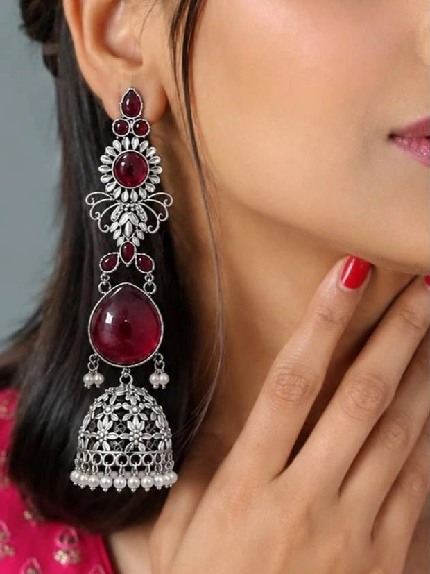 Close-up of a long oxidised silver jhumka with ruby stone layers and floral detailing worn on ear