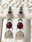 Pair of ruby and green stone jhumka earrings displayed on a white carved wooden frame