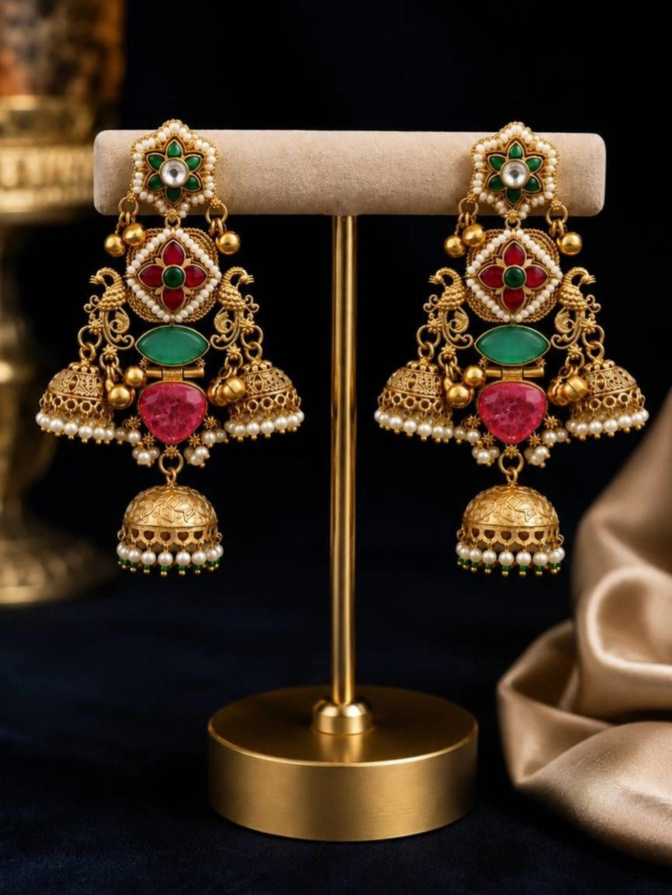 Pair of gold-plated jhumka earrings displayed on beige jewellery stand against dark background
