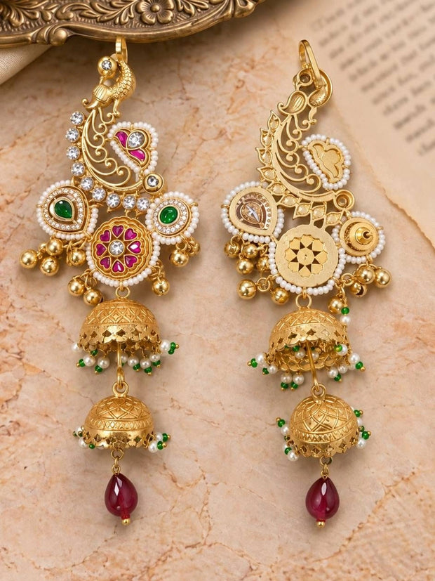 Front and back view of gold-plated peacock jhumka earrings laid flat on a marble surface