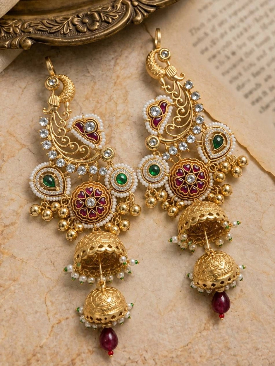 Gold peacock chandbali double jhumka earring worn on a womans ear with white flower hair accessory