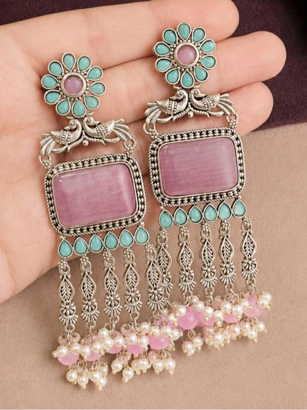 Pair of oxidised silver chandbali earrings with pink cat-eye stone and pearl tassel drops held in a woman's palm