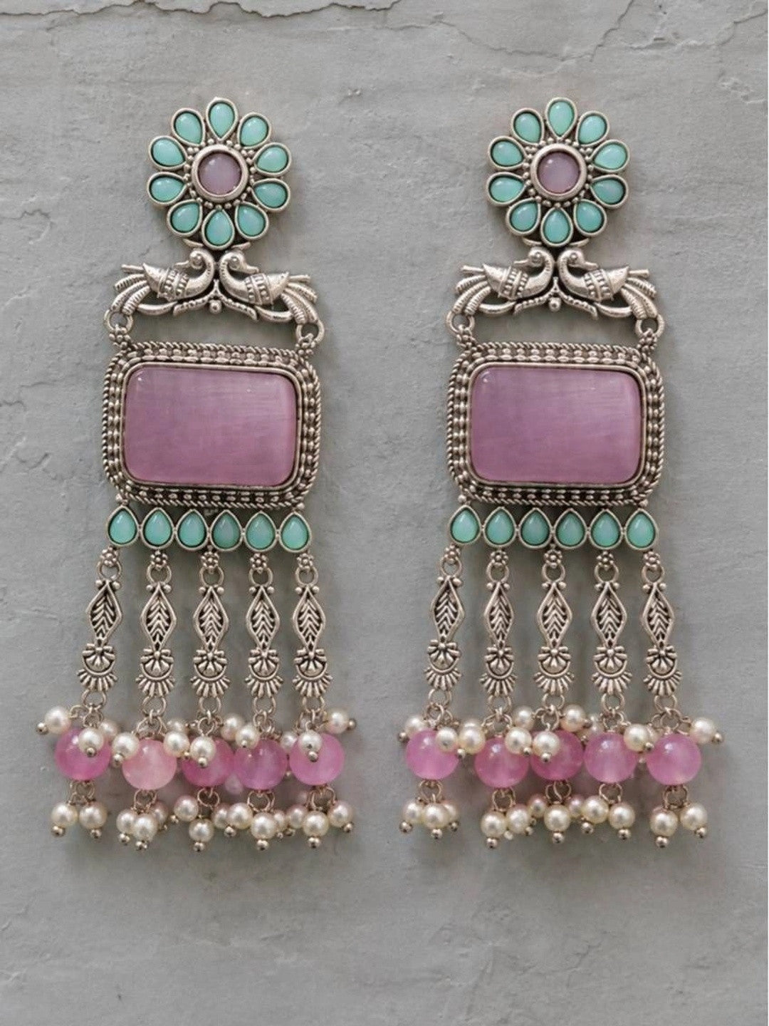 Front view of oxidised silver chandbali earrings with turquoise teardrop accents and pink bead tassels on a grey surface