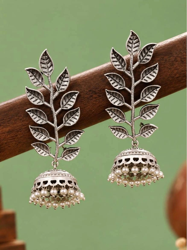 Pair of oxidised silver leaf jhumka earrings with pearl drops displayed on a wooden rod against green background