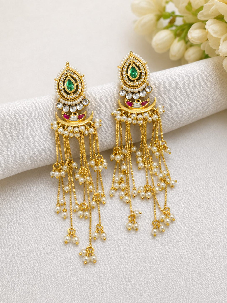 Pair of gold-plated kundan chandbali earrings with green stone and pearl tassel drops on white fabric