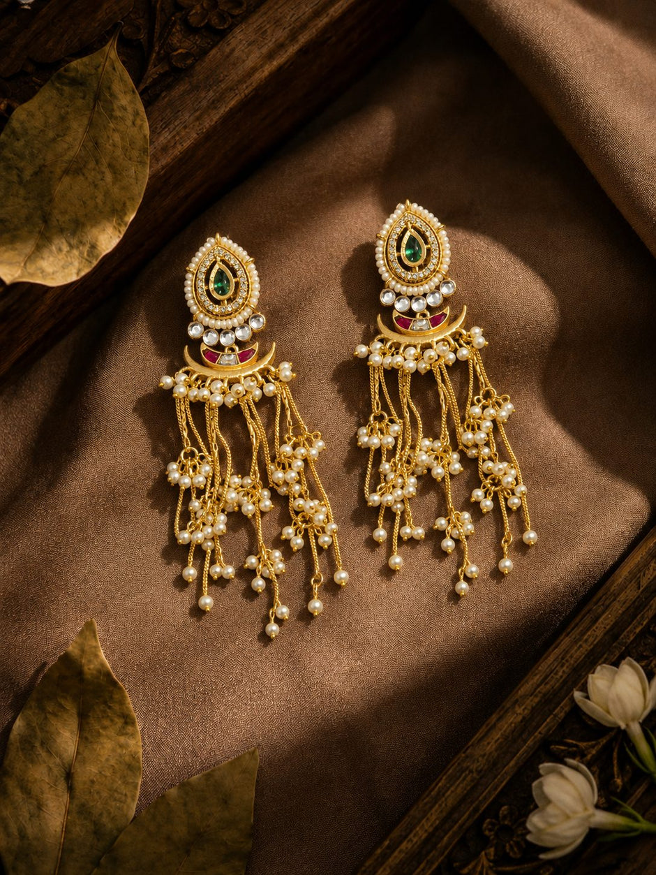Gold kundan chandbali earrings with pearl tassels resting on bronze silk fabric with jasmine flowers