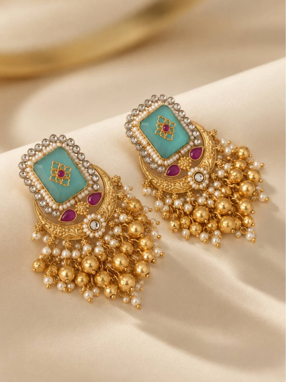 Close-up of two gold chandbali earrings showing aqua centre, ruby accents and cascading pearl and gold ball fringe
