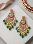Two gold-plated kundan chandbali earrings laid flat on white stone surface showing front face with pearl clusters and green drop beads
