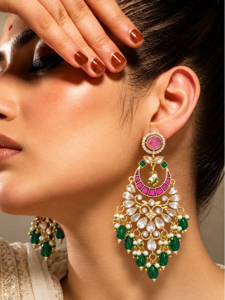 Woman wearing gold-plated kundan chandbali earring with pink cabochon stud, fuchsia stone crescent and cascading emerald bead drops against a warm studio background