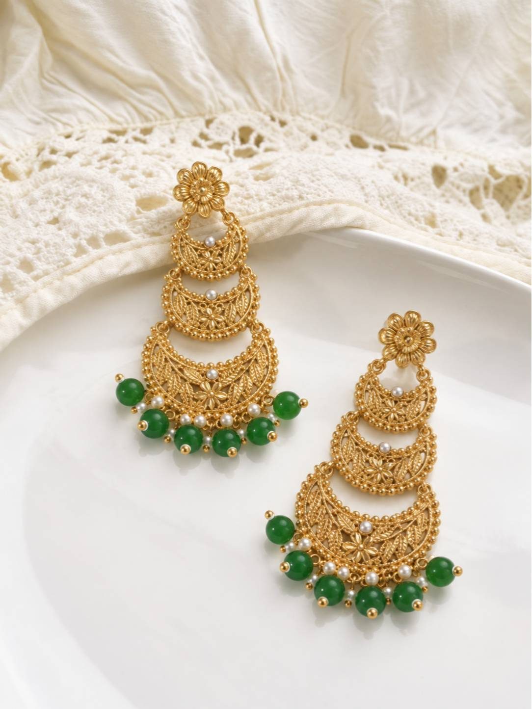 Both gold-plated chandbali earrings with green and pearl drops resting on a white ceramic plate