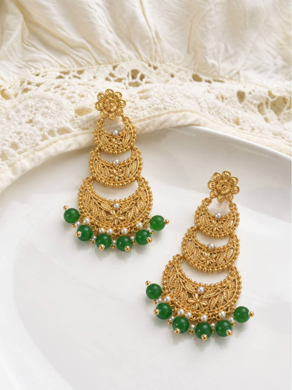 Both gold-plated chandbali earrings with green and pearl drops resting on a white ceramic plate