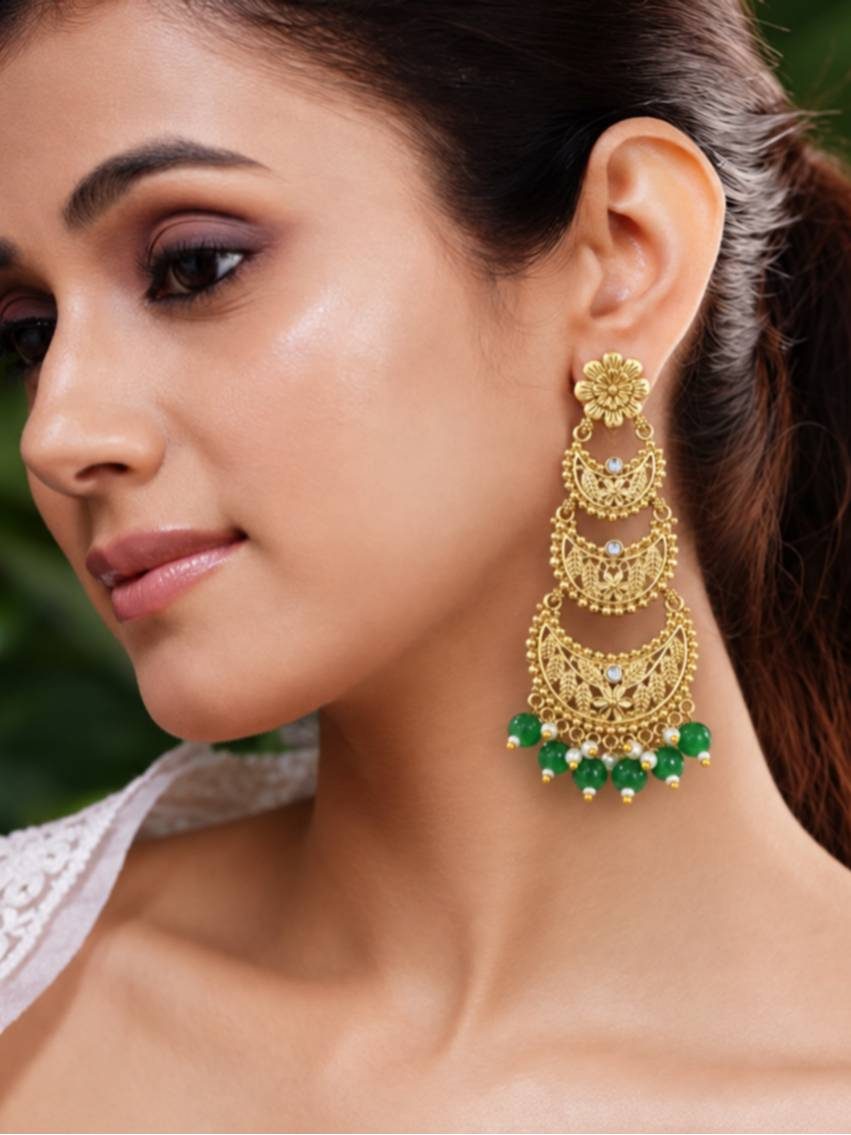 Woman wearing one gold-plated chandbali earring with green bead drops against a natural background