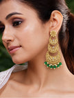 Woman wearing one gold-plated chandbali earring with green bead drops against a natural background