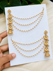 Both gold-plated pearl hair chain jhumka earrings displayed on a white card held by a hand against green leaves