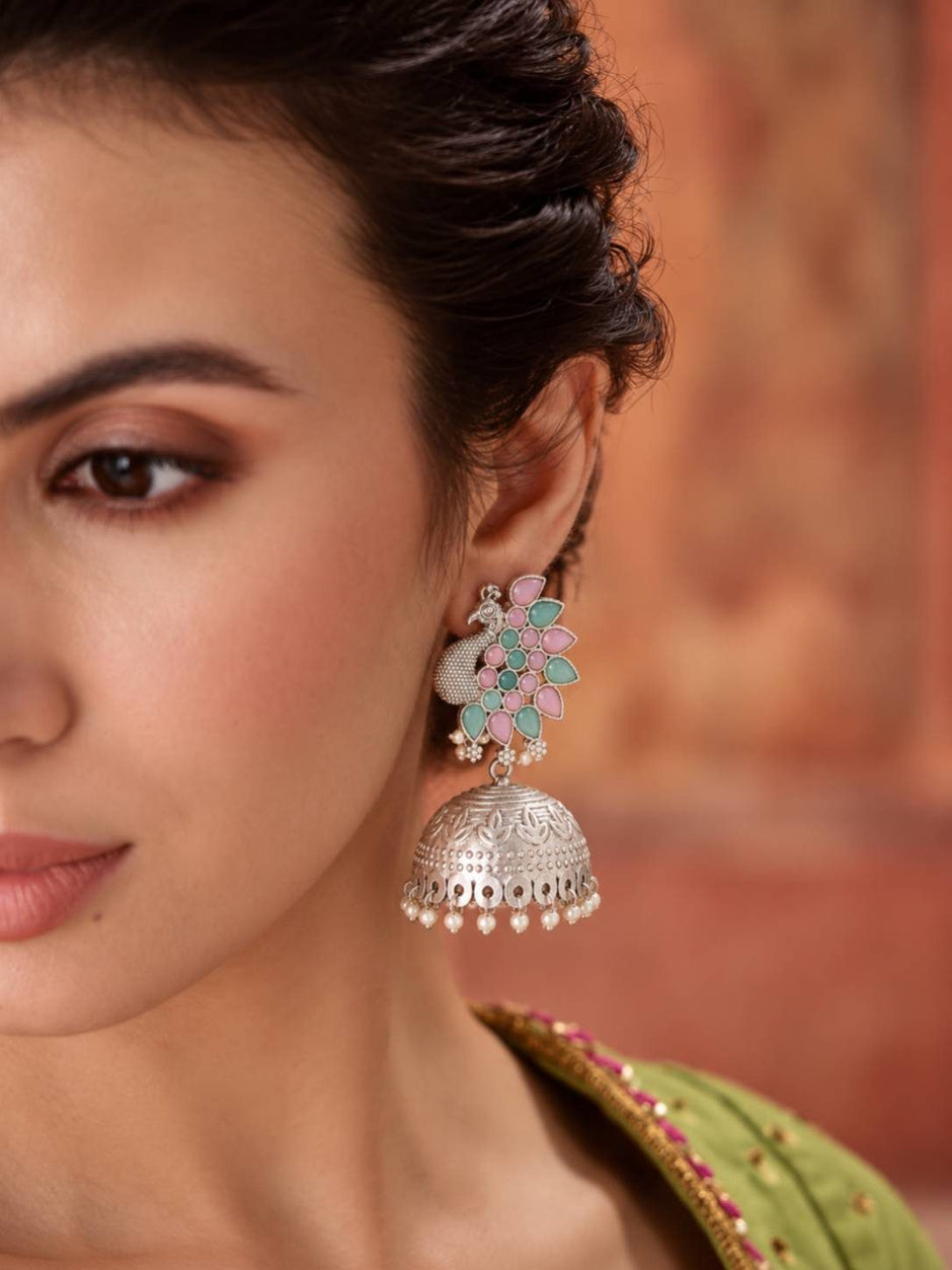 Woman wearing a single oxidised silver peacock jhumka earring with green and pink stones and pearl drops