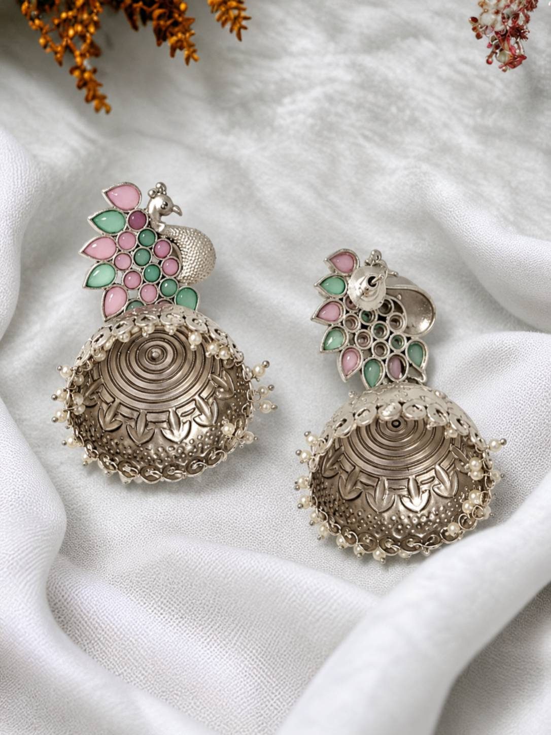 Side-angle view of oxidised silver peacock jhumka earrings on white fabric showing circular engraving detail