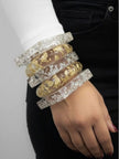 Five clear resin bangles stacked on a woman's wrist showing gold and silver foil inclusions against a white sleeve and black jeans