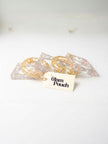 Five clear resin bangles with gold and silver foil arranged loosely on a white surface beside a Glam Pouch branded tag