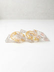 Close-up of five clear resin bangles in square and oval silhouettes showing embedded metallic foil on a white background
