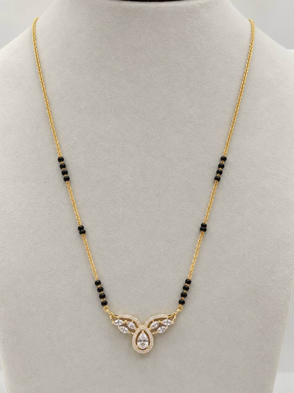 Gold-plated mangalsutra with CZ pear pendant and black beads displayed on a white jewellery bust
