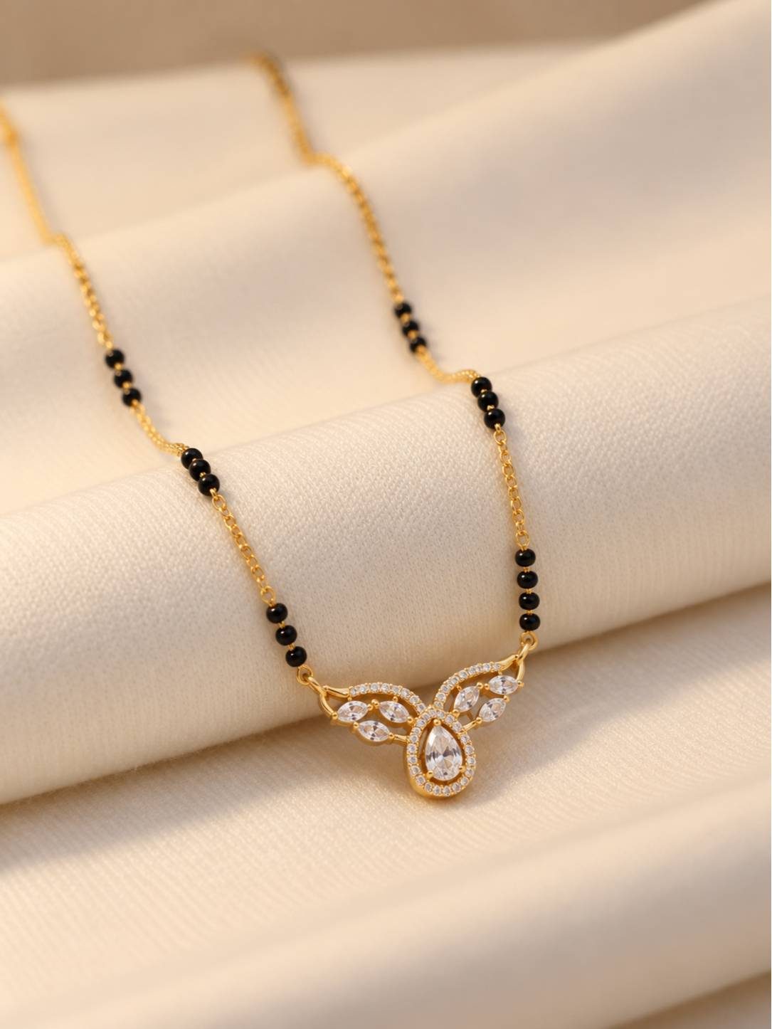 Close-up of CZ stone mangalsutra pendant with marquise accents resting on cream fabric