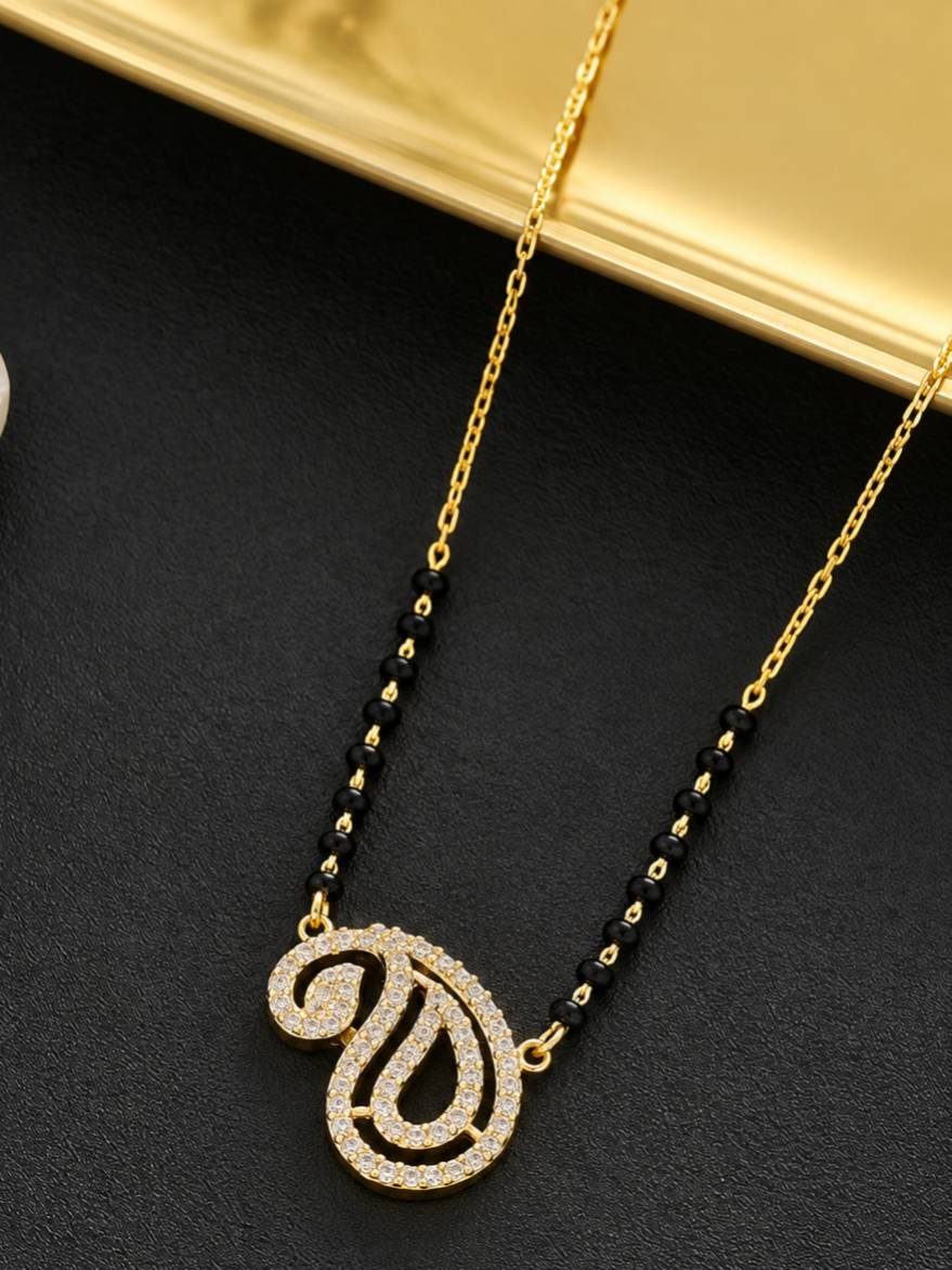 Close-up of CZ-studded paisley mangalsutra pendant on black bead and gold chain against dark background