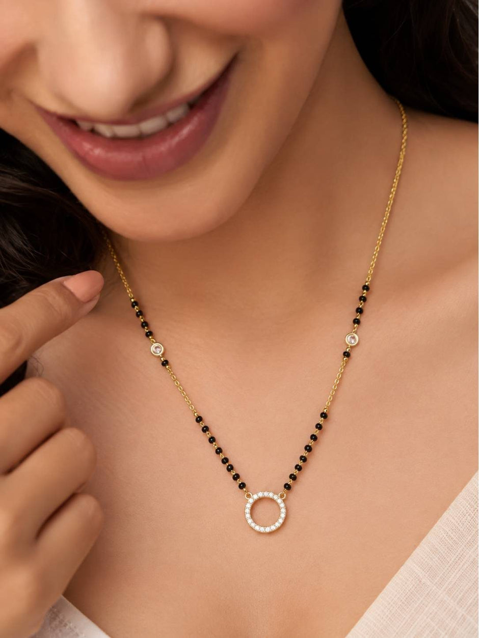 Woman wearing gold-plated CZ halo pendant mangalsutra with black beads against a cream outfit