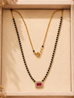 Gold-plated black bead mangalsutra with fuchsia CZ square pendant displayed flat in a cream jewellery box