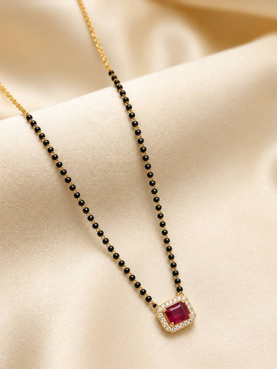 Close-up of mangalsutra draped on ivory satin fabric showing black bead chain and ruby CZ halo pendant