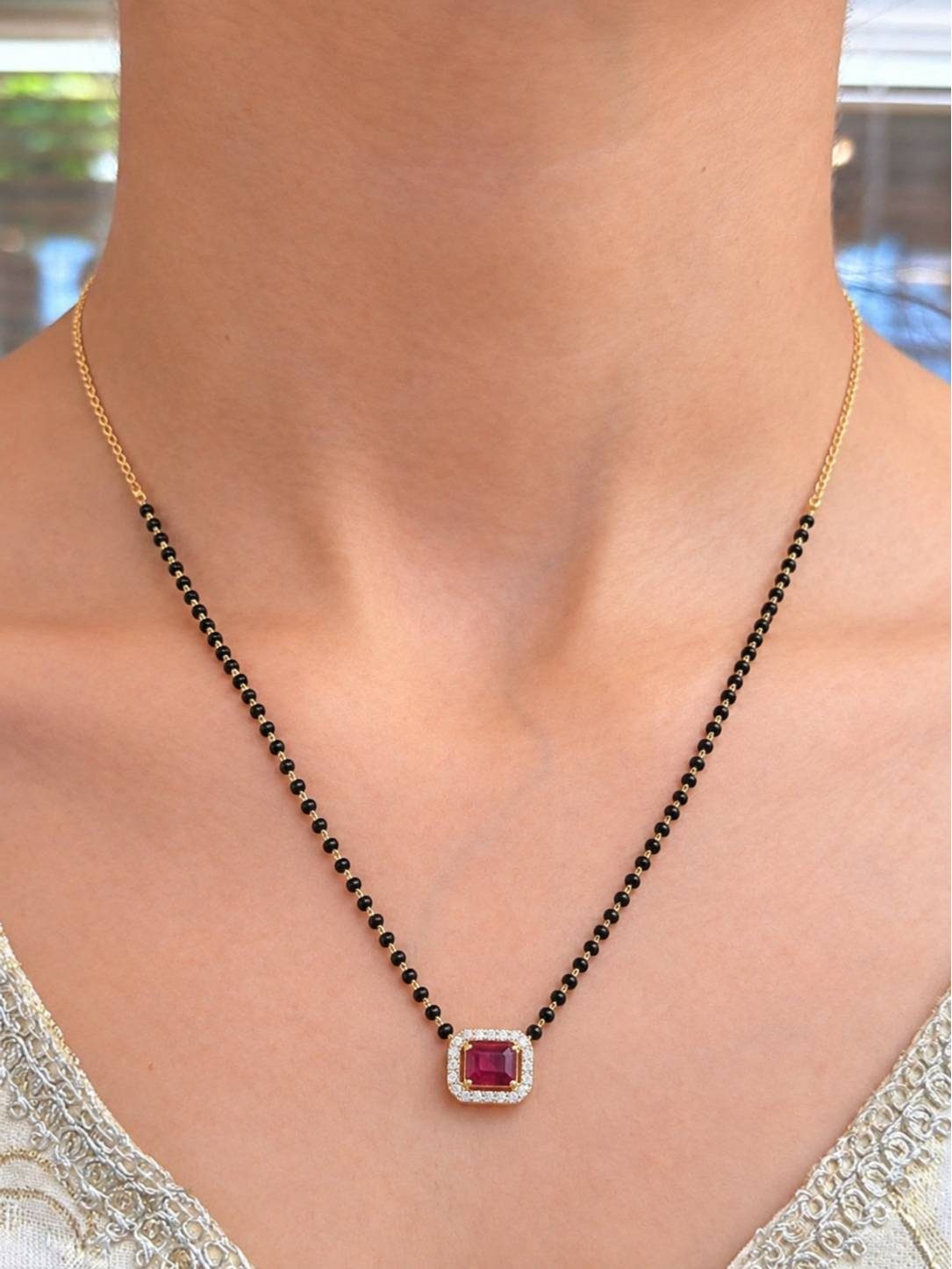 Model wearing gold-plated black bead mangalsutra with ruby CZ pendant over a white embroidered neckline