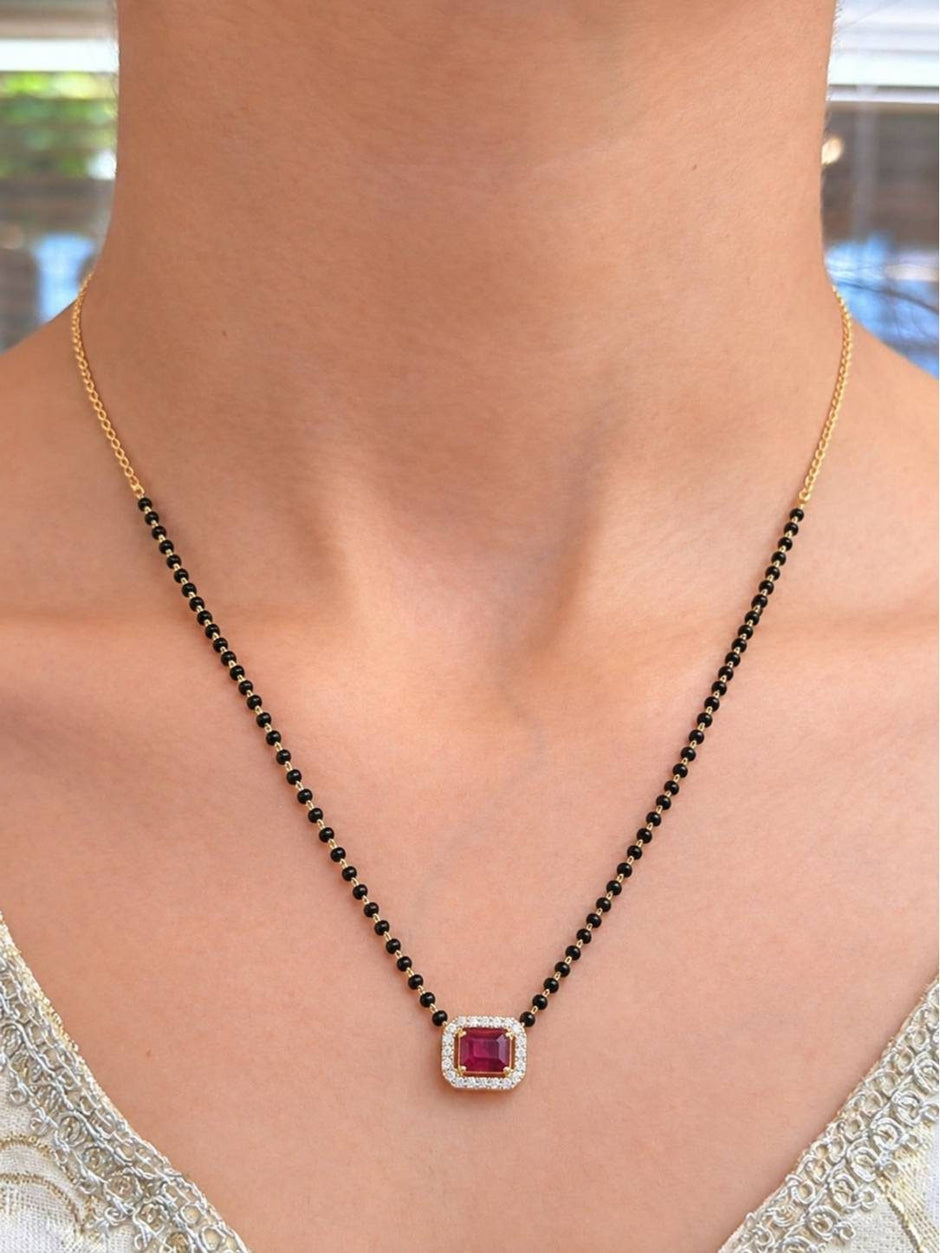 Model wearing gold-plated black bead mangalsutra with ruby CZ pendant over a white embroidered neckline