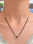 Model wearing gold-plated black bead mangalsutra with ruby CZ pendant over a white embroidered neckline
