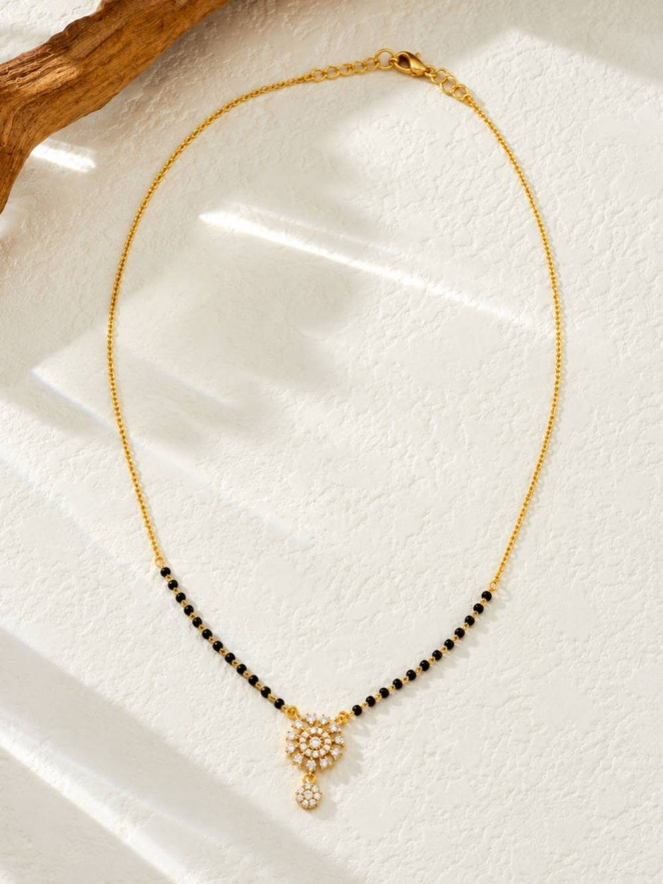 Full view of gold-plated black bead mangalsutra with cubic zirconia floral pendant on a white surface