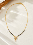 Full view of gold-plated black bead mangalsutra with cubic zirconia floral pendant on a white surface